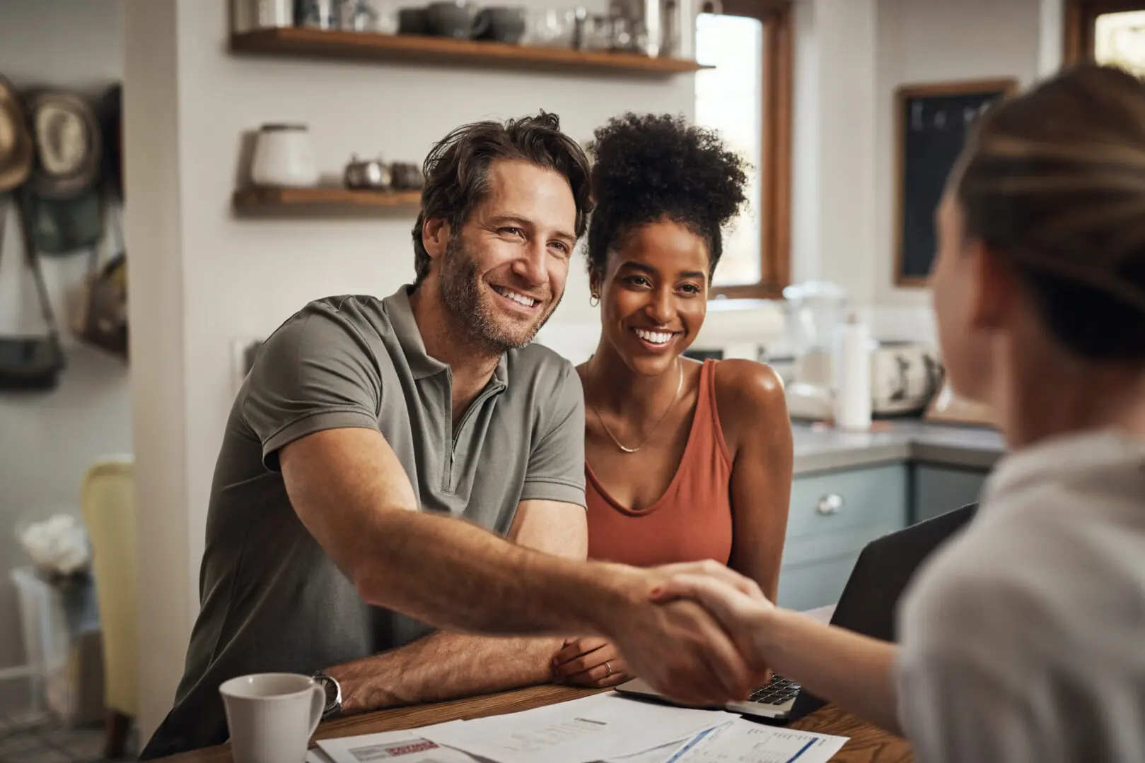 A happy couple shaking hands with someone in a cozy kitchen setting.