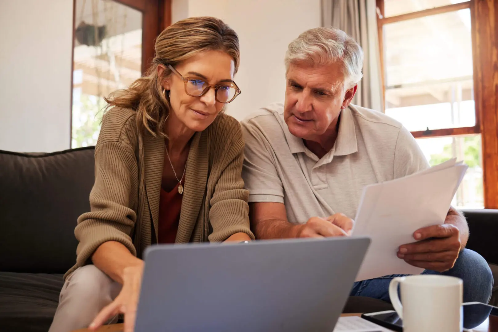 A middle-aged couple looking intently at a laptop screen, discussing something together in a cozy room.