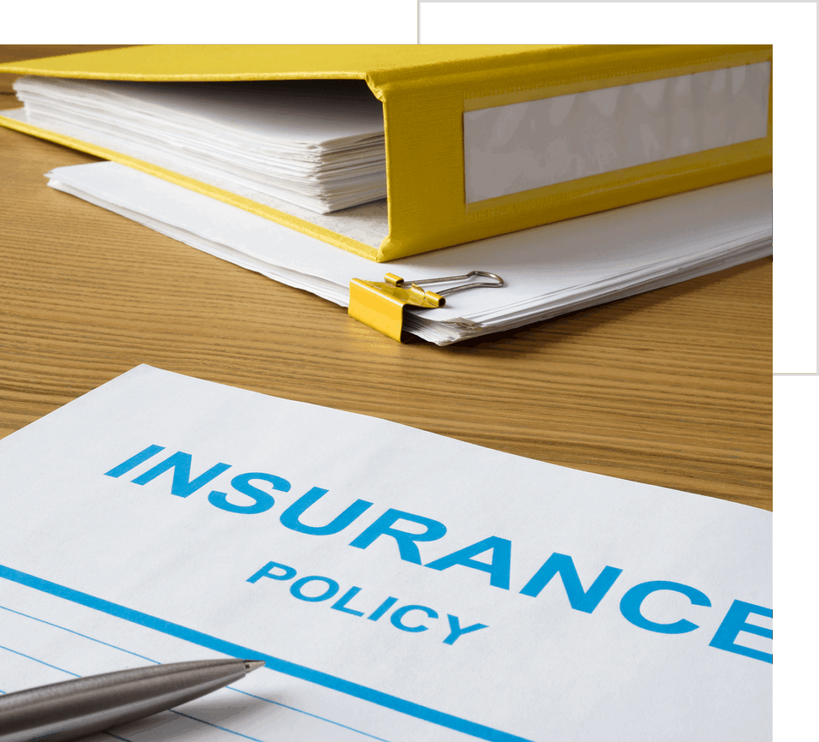 A yellow binder and stacks of documents next to an insurance policy paper on a wooden desk.