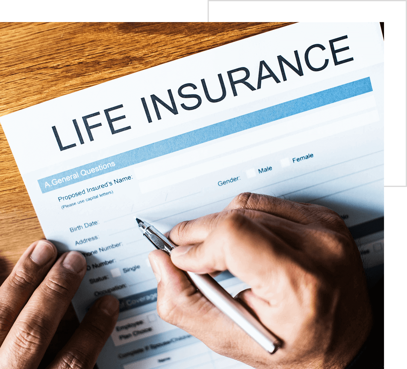 A person filling out a life insurance application form with a pen on a wooden table.