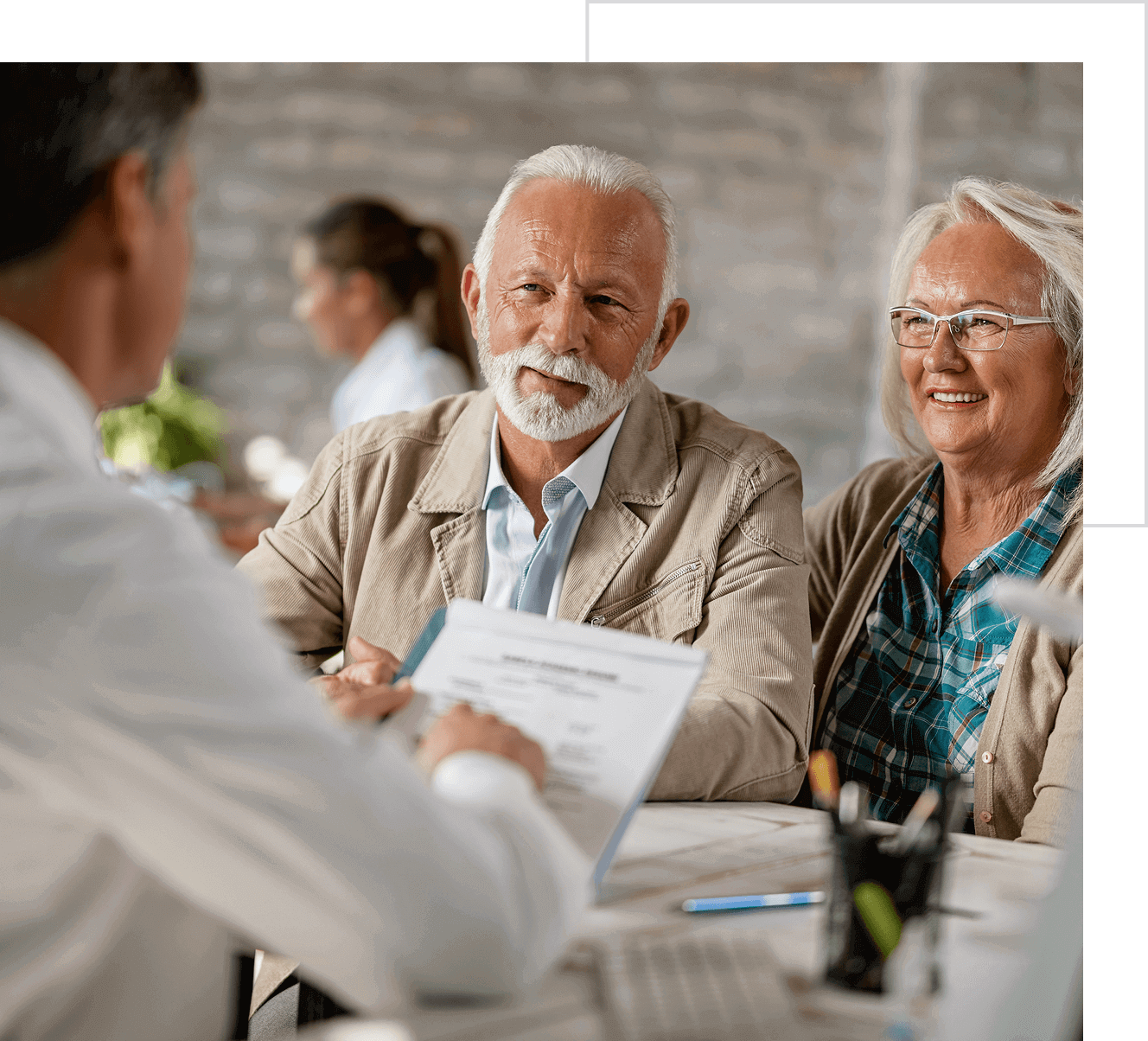 An elderly couple consulting with a professional in an office setting, discussing documents and smiling.