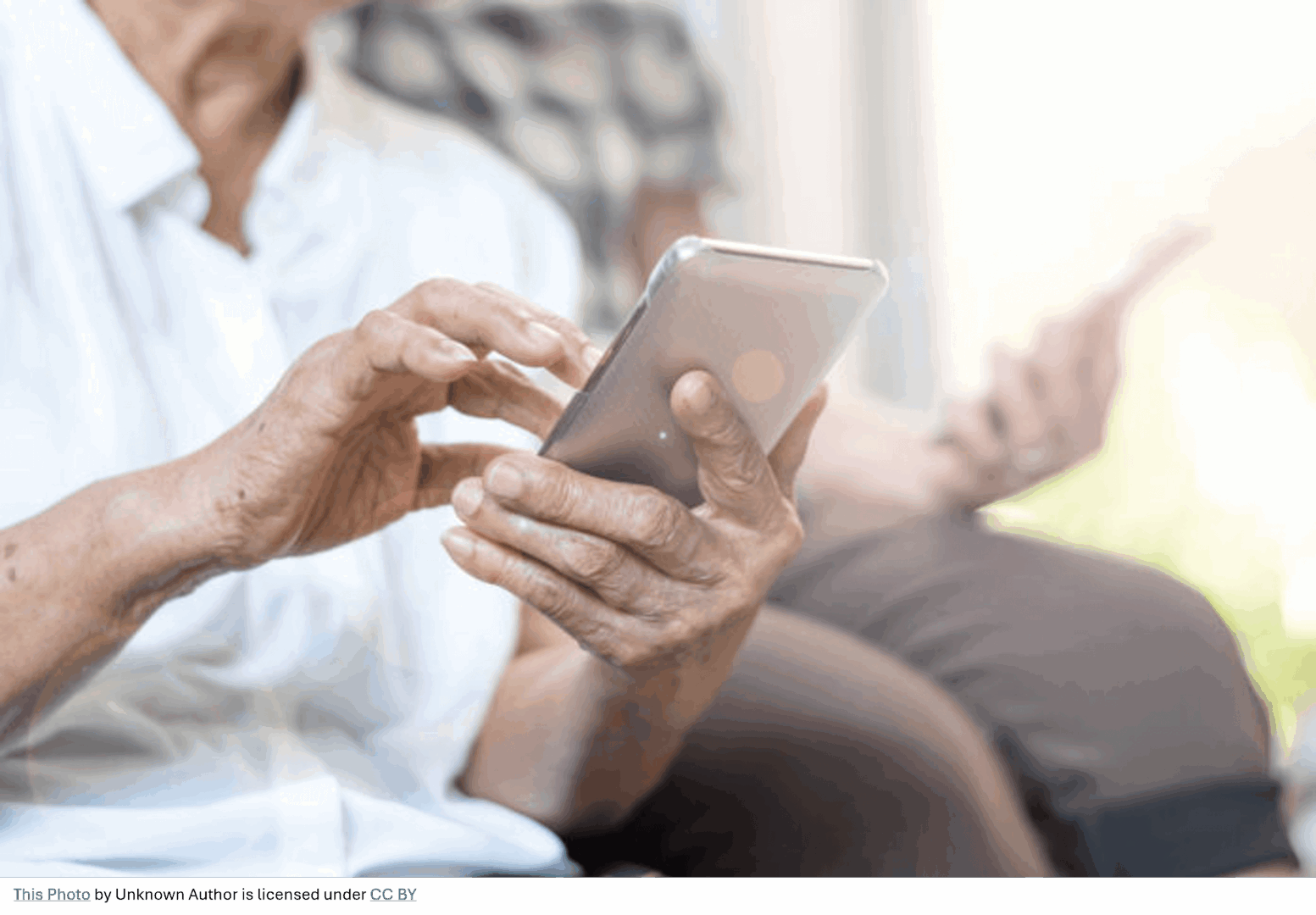 Close-up of an elderly person using a smartphone with a blurred background of another person sitting nearby.