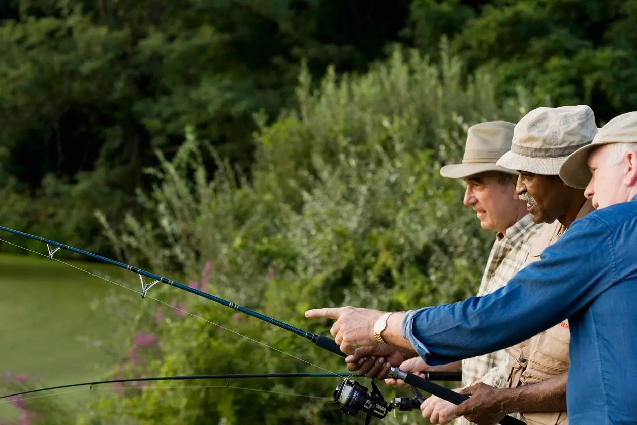 Two men fishing together, each holding a fishing rod, surrounded by lush greenery.