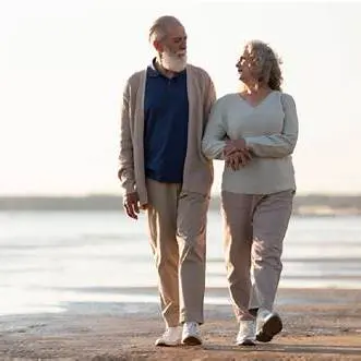 An elderly couple walking arm in arm along a beach during sunset, enjoying a peaceful moment together.