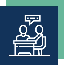 Two stick figures at a desk, one speaking, in a consultation or interview setting.