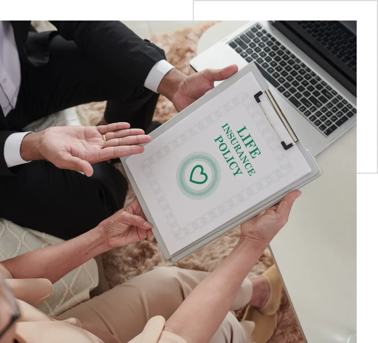 Two people reviewing a life insurance policy document on a clipboard, sitting next to a laptop on a table.
