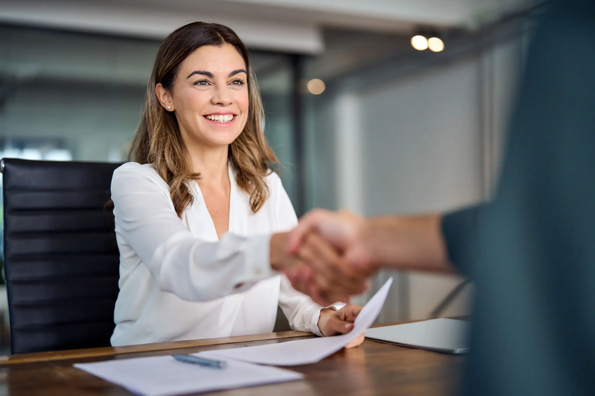 A smiling businesswoman shaking hands with a colleague during a meeting in a modern office.